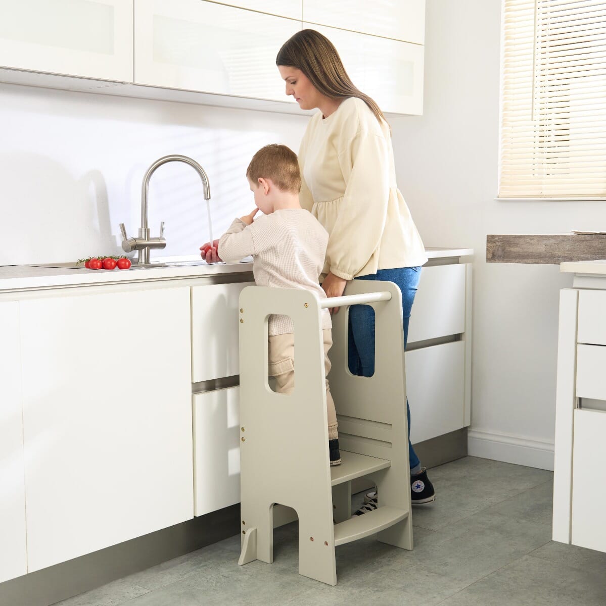 Mother supervises child at counter with the Helping Hands Montessori learning tower in mushroom finish, encouraging hands-on kitchen learning.