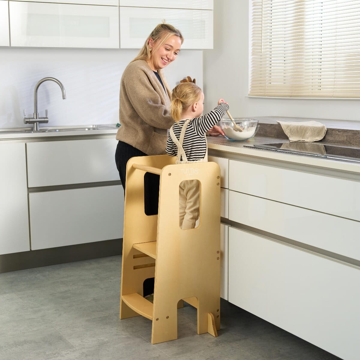 Mum supervises toddler standing safely in the Helping Hands Montessori learning tower in natural finish, perfect for interactive family activities