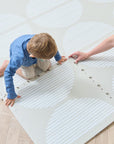 A child and a woman connecting the pieces of the Orbital oatmeal infinity playmat.
