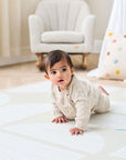 Baby crawling on the Orbital Oatmeal infinity playmat on a neutral bedroom with a rocking chair on the background.