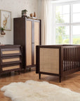 Japandi 3-piece nursery set in warm walnut finish, featuring a cot bed, rattan-panelled wardrobe, and matching chest changer in a styled nursery room, blending natural textures with functional design.
