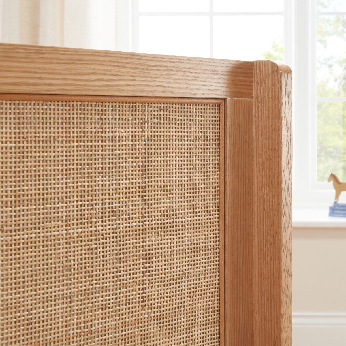 Side panel close-up of the Japandi Mini Cot Bed in light oak, showcasing textured rattan and smooth curved wooden edge.