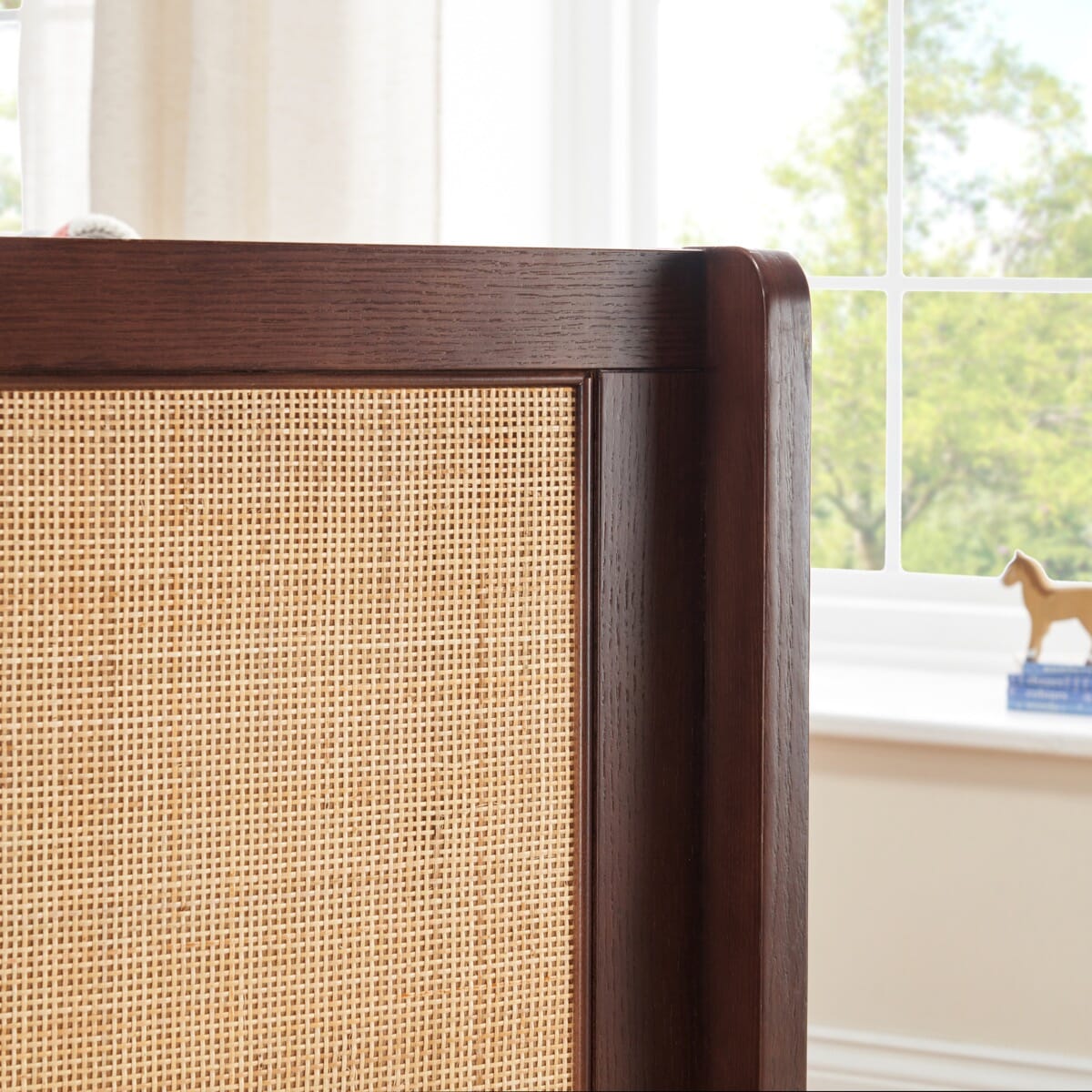 Japandi Mini Cot Bed in warm walnut close-up showing woven rattan side panel. Combines natural textures with solid wood highlighting expert craftsmanship.