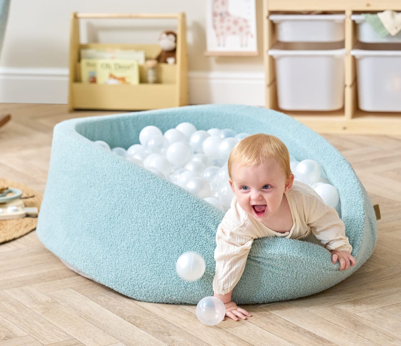 Baby climbing out of the Bola baby ball pit in ocean stone during active play, showing flexible sides and a safe, cushioned design