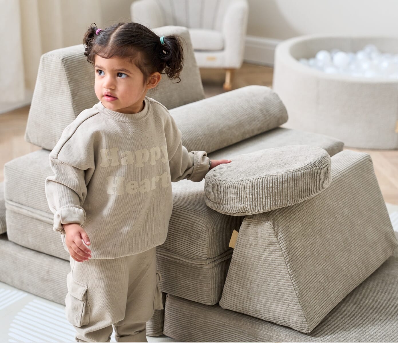 Toddler standing beside the Playrama kids play sofa in mushroom, showing soft corduroy texture and supportive modular blocks for play