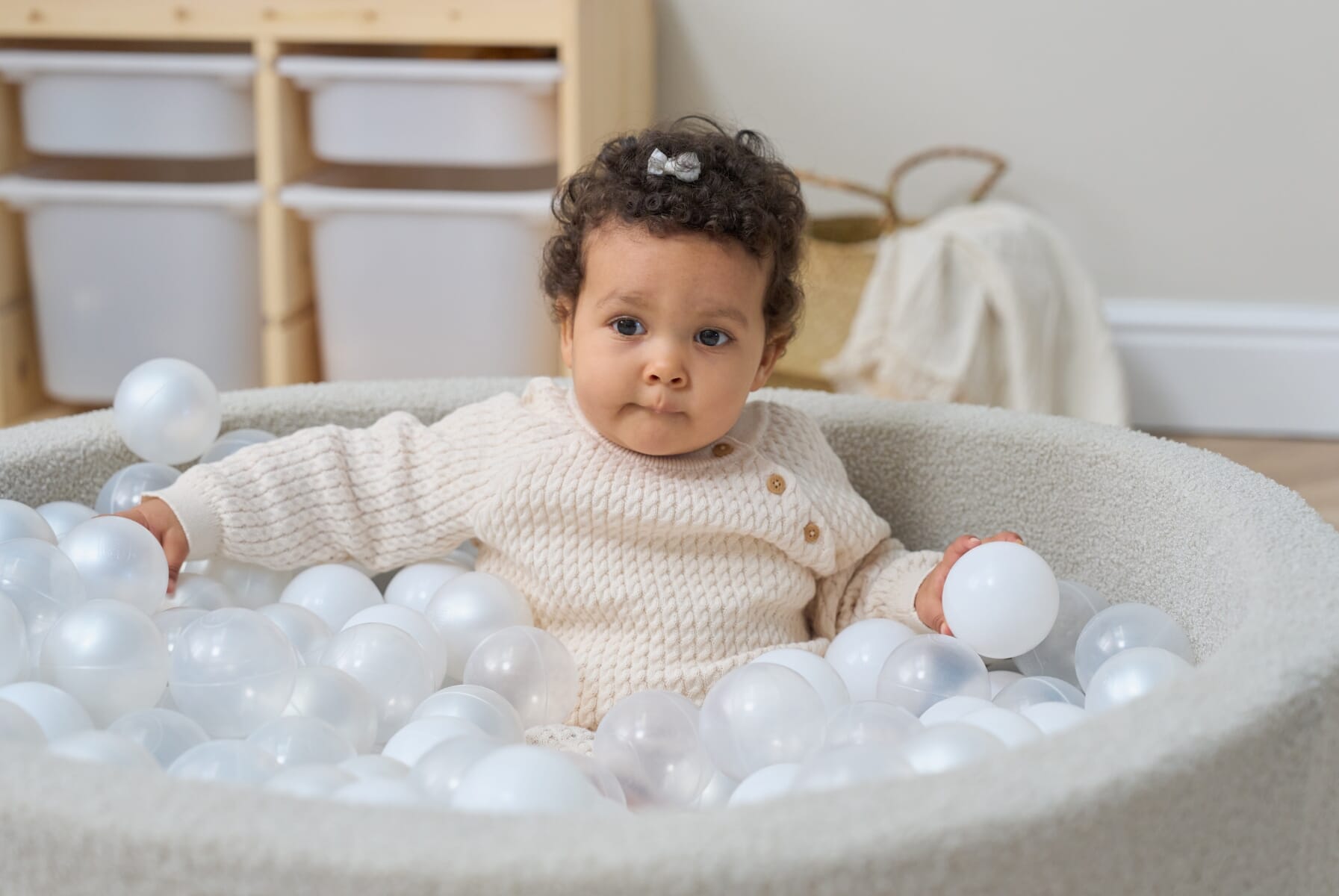 Baby seated inside the Bola baby ball pit in mushroom, surrounded by soft white balls that encourage sensory exploration and movement