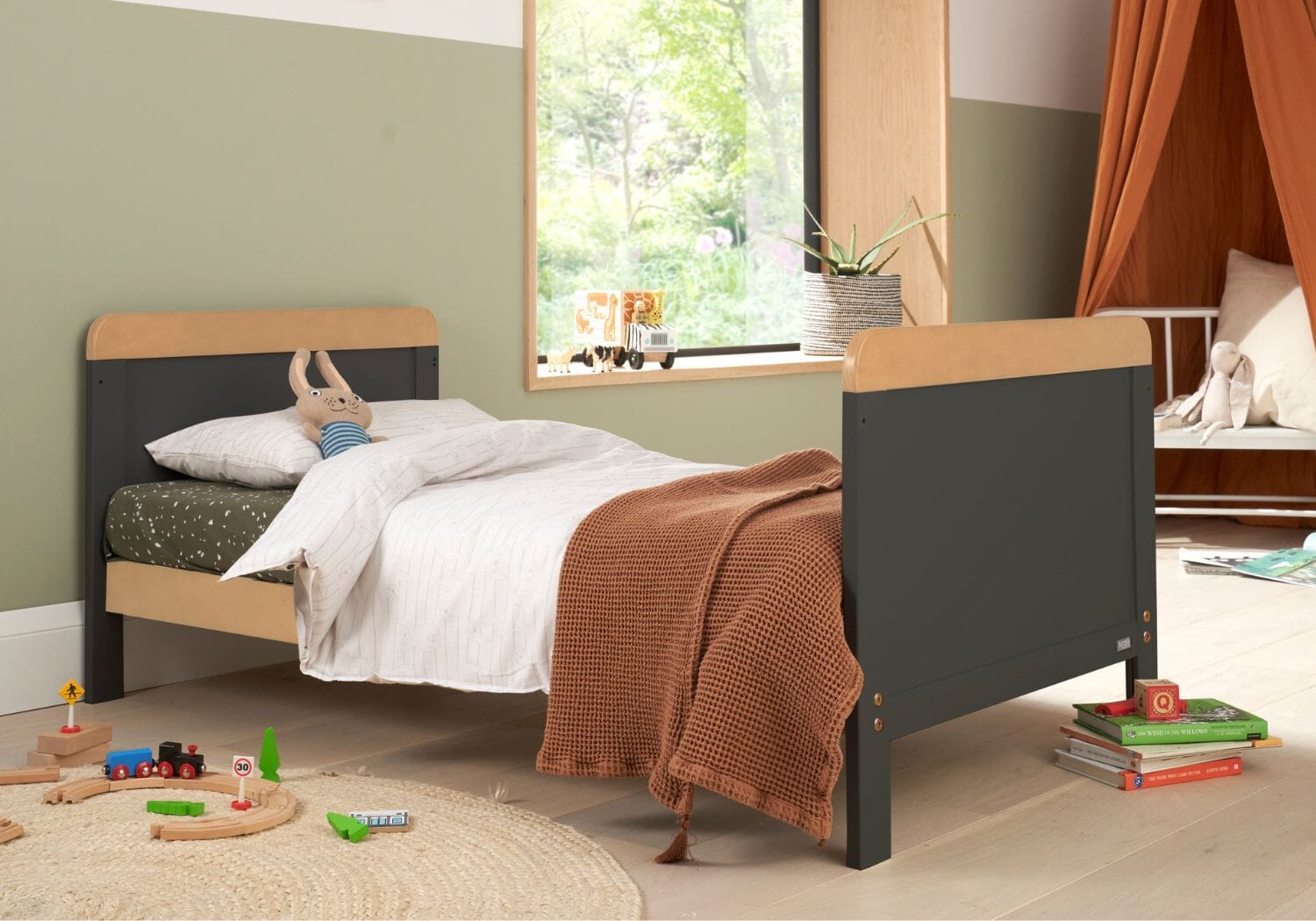 Lifestyle view of the Rio cot bed in slate grey and honey oak styled as a toddler bed, featuring soft bedding and playful room décor