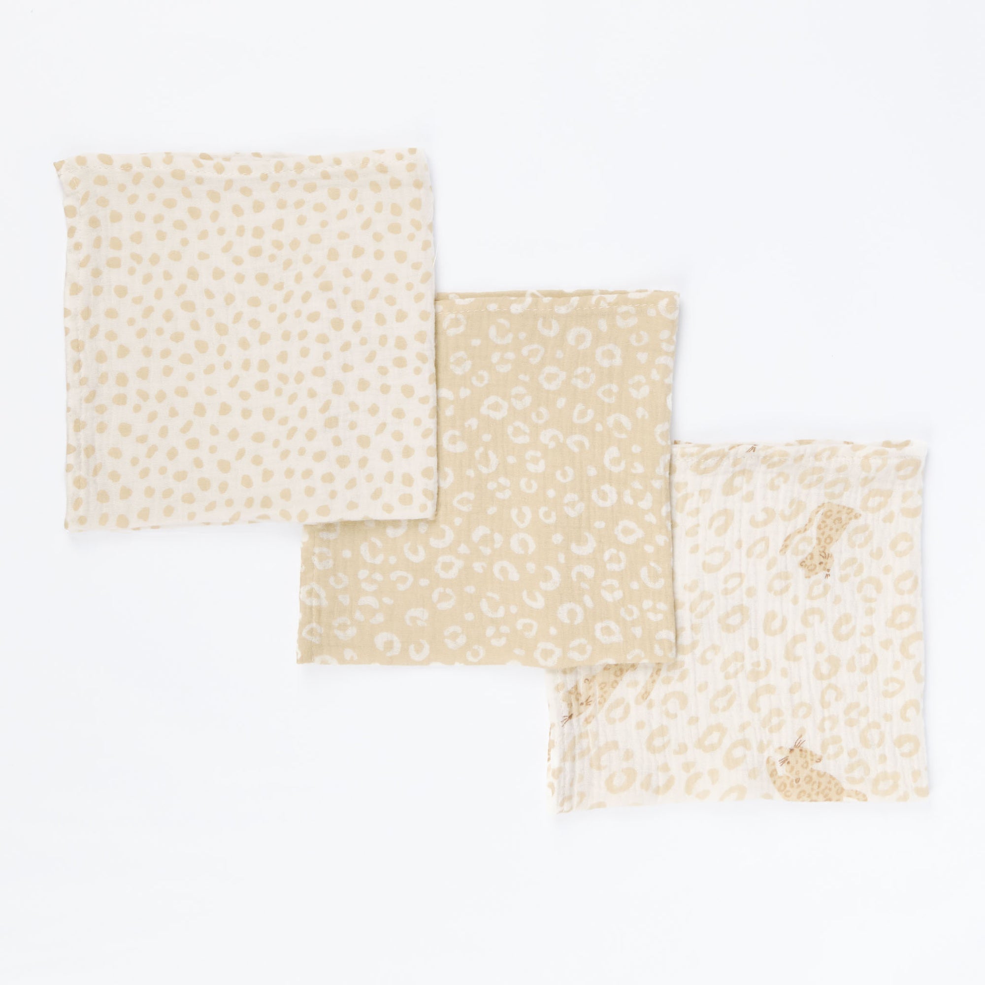 Flat lay of three Love Cats large muslin swaddles in coordinating beige and cream prints, featuring spots, leopard motifs, and natural hues