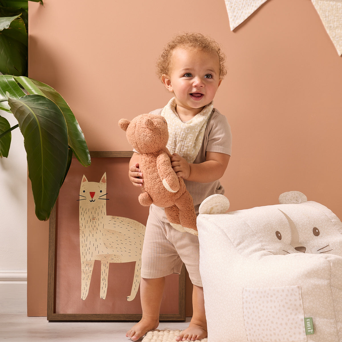 Toddler standing beside the Luca Leopard beanbag chair in cream leopard print, holding a teddy in a warm, playful nursery setting