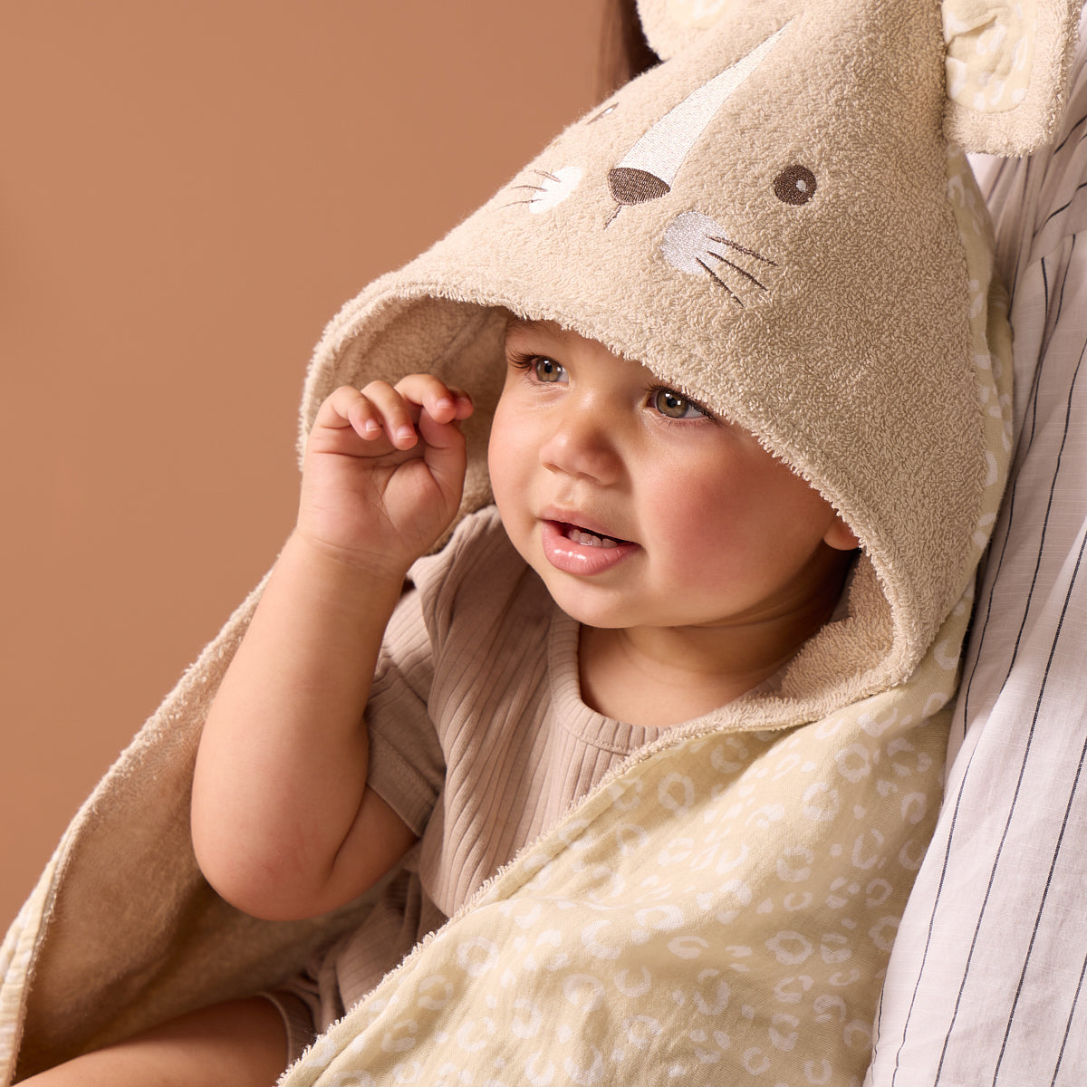 Close-up of toddler wrapped in Luca Leopard hooded towel, showing embroidered whiskers, 3D ears, and gentle beige leopard print lining