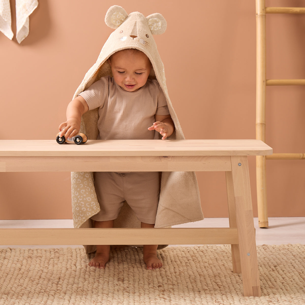 Toddler playing with toy car while wearing the Luca Leopard hooded towel in soft beige terry, lined with subtle leopard print cotton