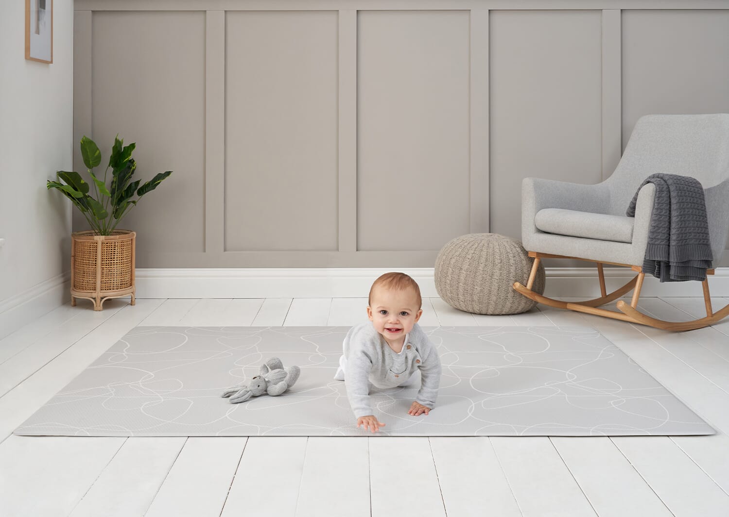 Baby crawling on the grey abstract play mat in a soft, neutral nursery, showing its padded support and calming, modern design