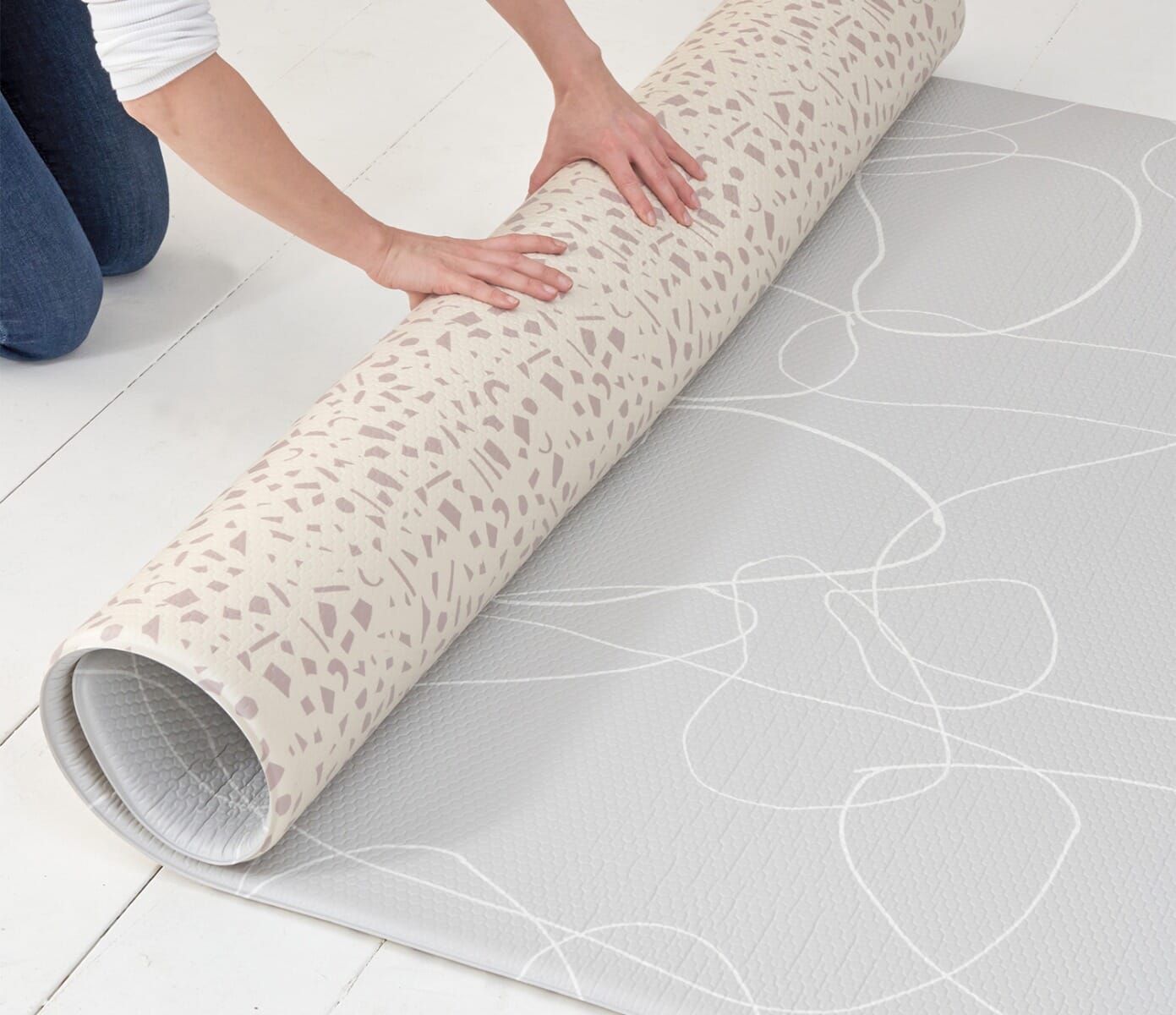 Hands rolling the reversible Bubble Terrazzo play mat to reveal its grey abstract side, showing flexible use and simple storage