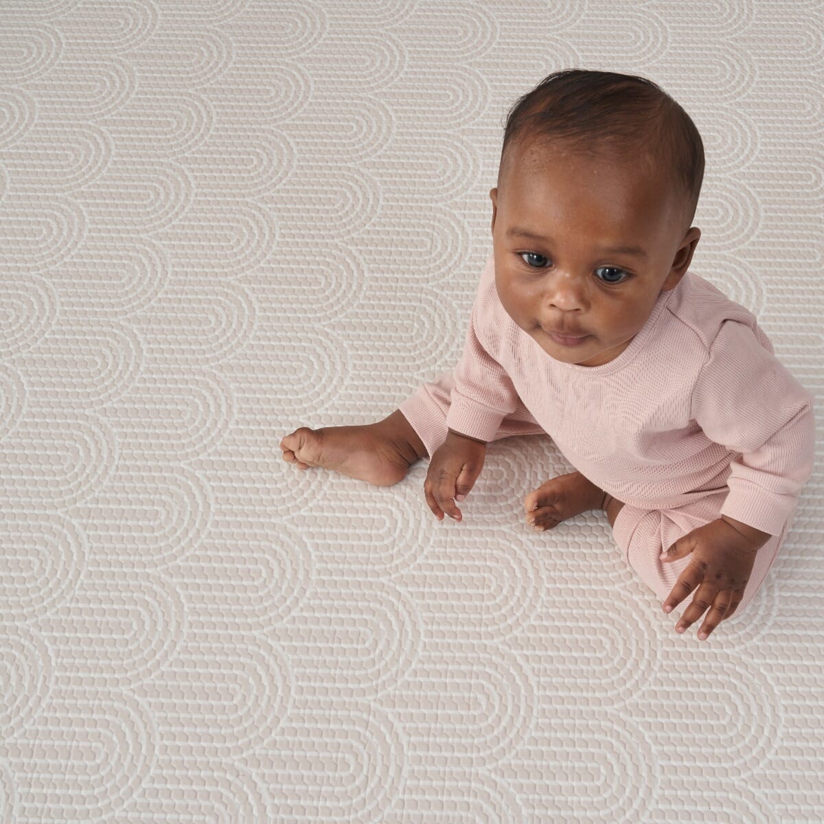 Close-up of a toddler sitting on the cathedral arch side of the mat, showing the raised pattern and soft, supportive padding beneath