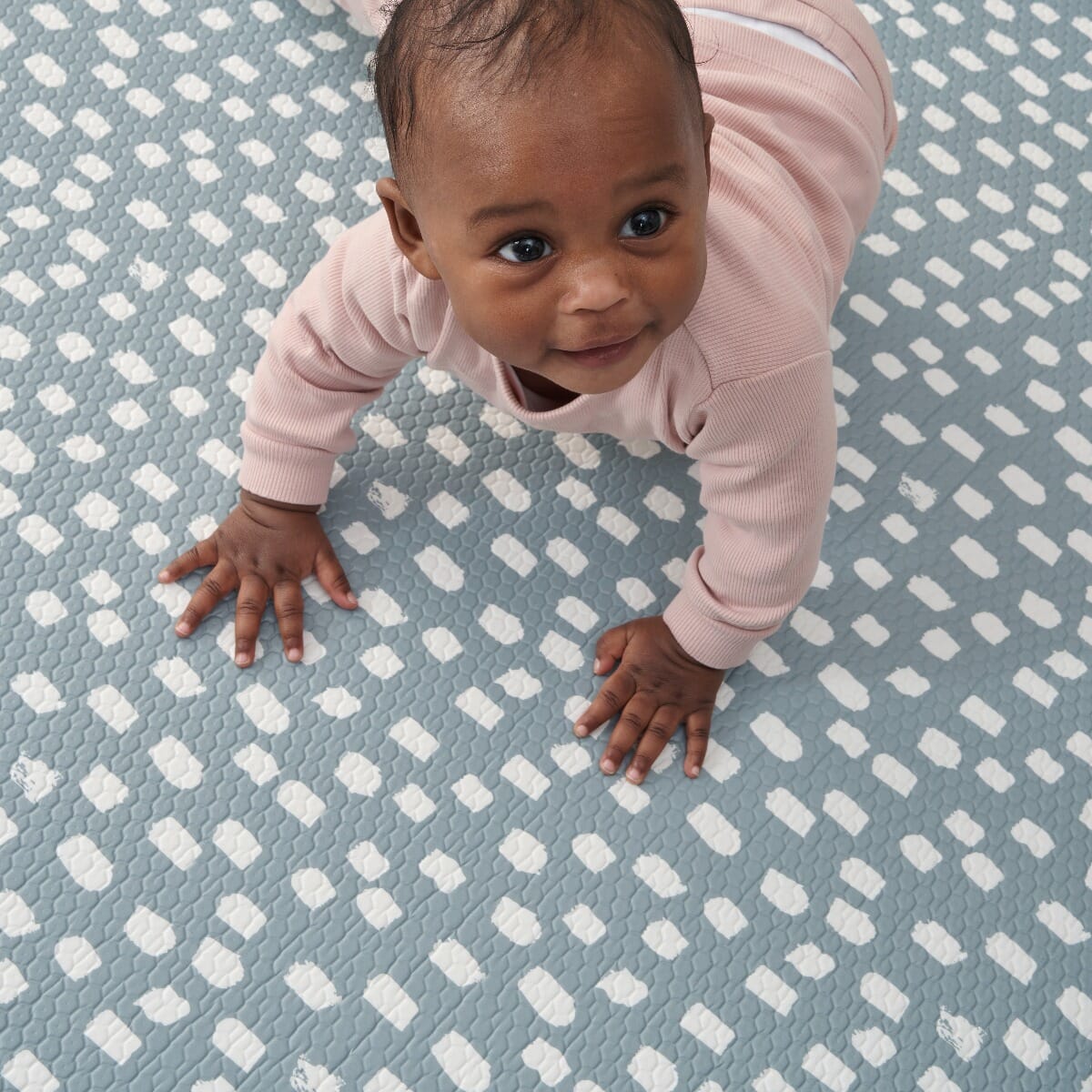 Toddler crawling on the blue dash side of the Cathedral &amp; Dash mat, showing cushioned support and a tactile surface for early movement