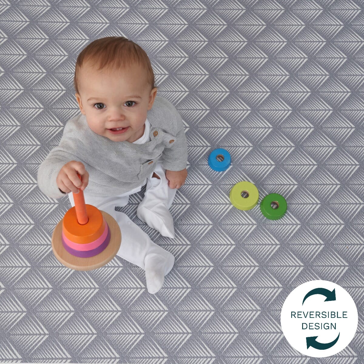 Toddler playing on the grey fan-pattern side of the reversible play mat, showing its cushioned surface for secure, engaging playtime