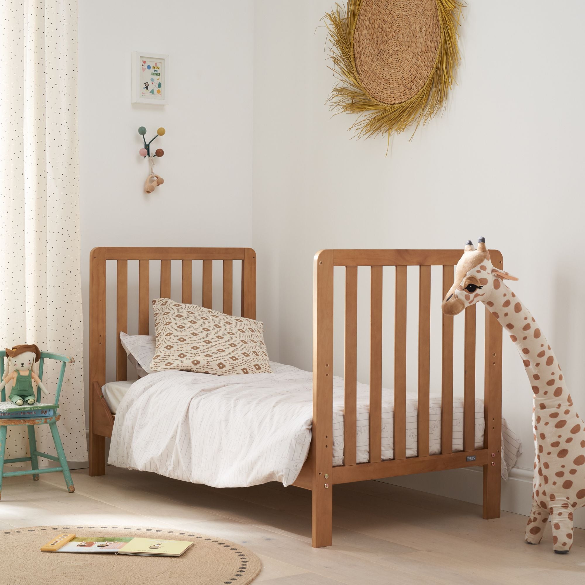 Toddler bed mode of the Malmo cot bed in oak styled in a modern nursery with bedding, toys, and gentle natural daylight