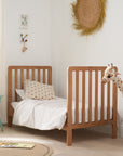 Toddler bed mode of the Malmo cot bed in oak styled in a modern nursery with bedding, toys, and gentle natural daylight