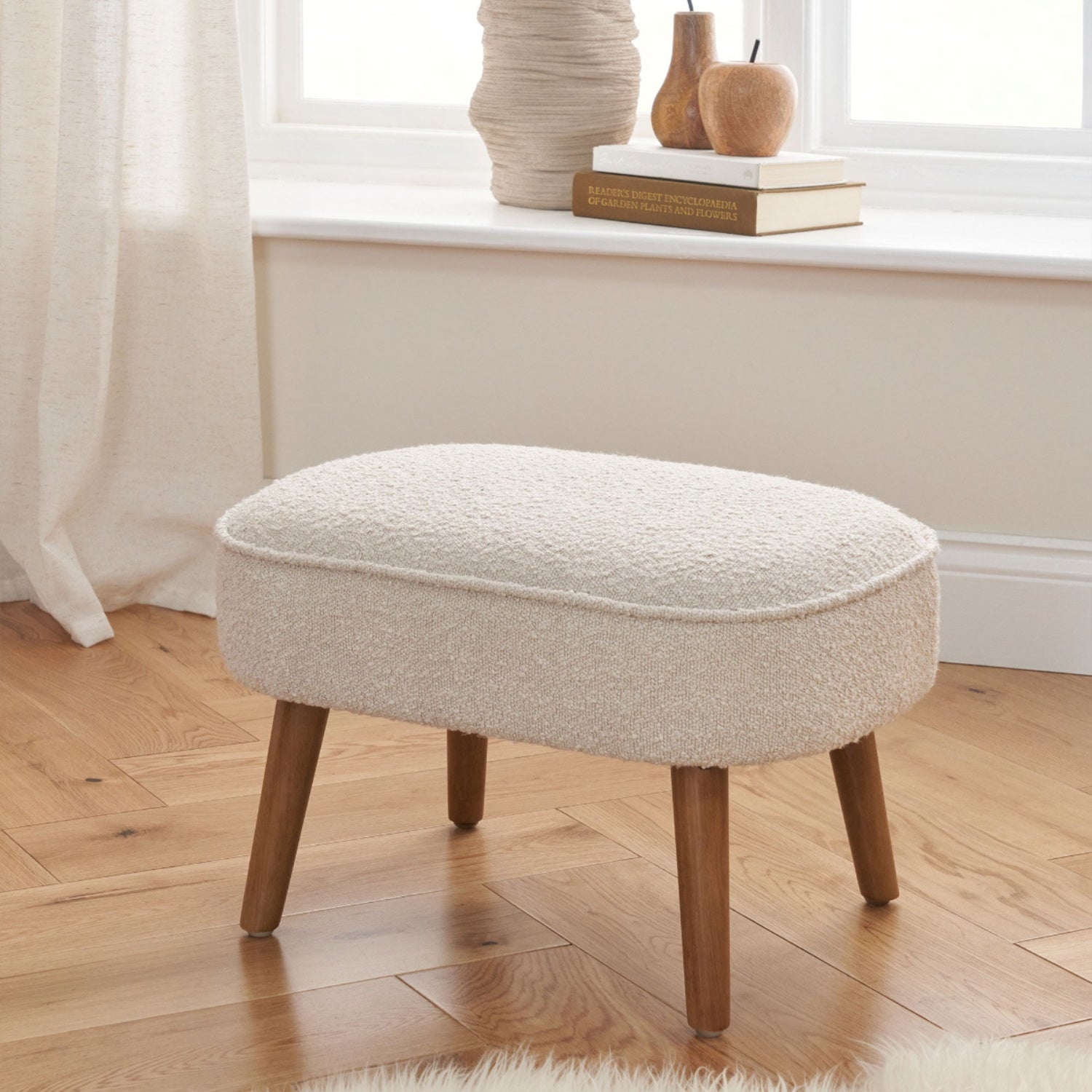 Micah footstool in biscuit boucle with wooden legs, styled in a cosy room setting with natural wood flooring.