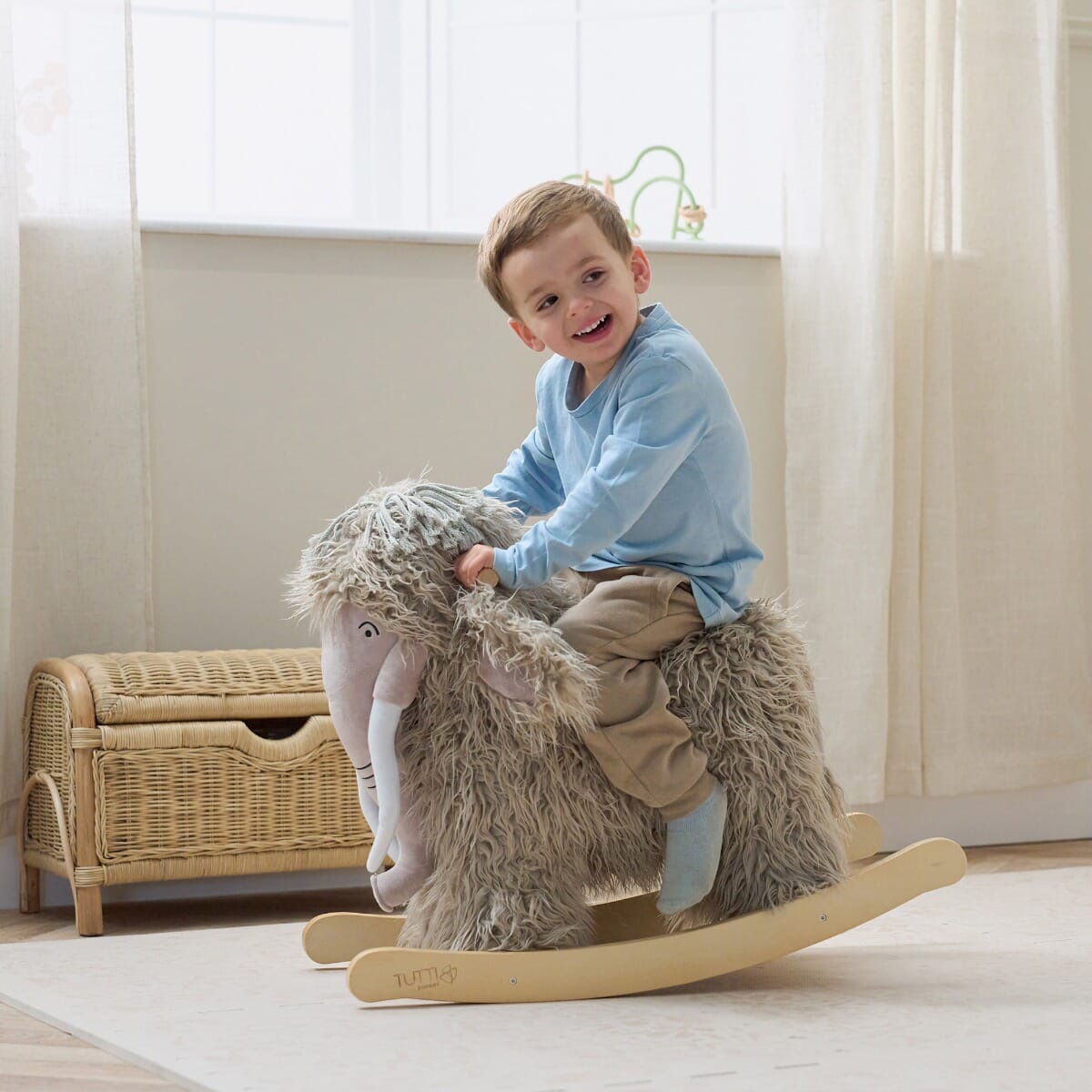 Lifestyle image of a toddler riding Mimi the Mammoth rocking toy, showing supportive handles, gentle rocking motion and playful scale