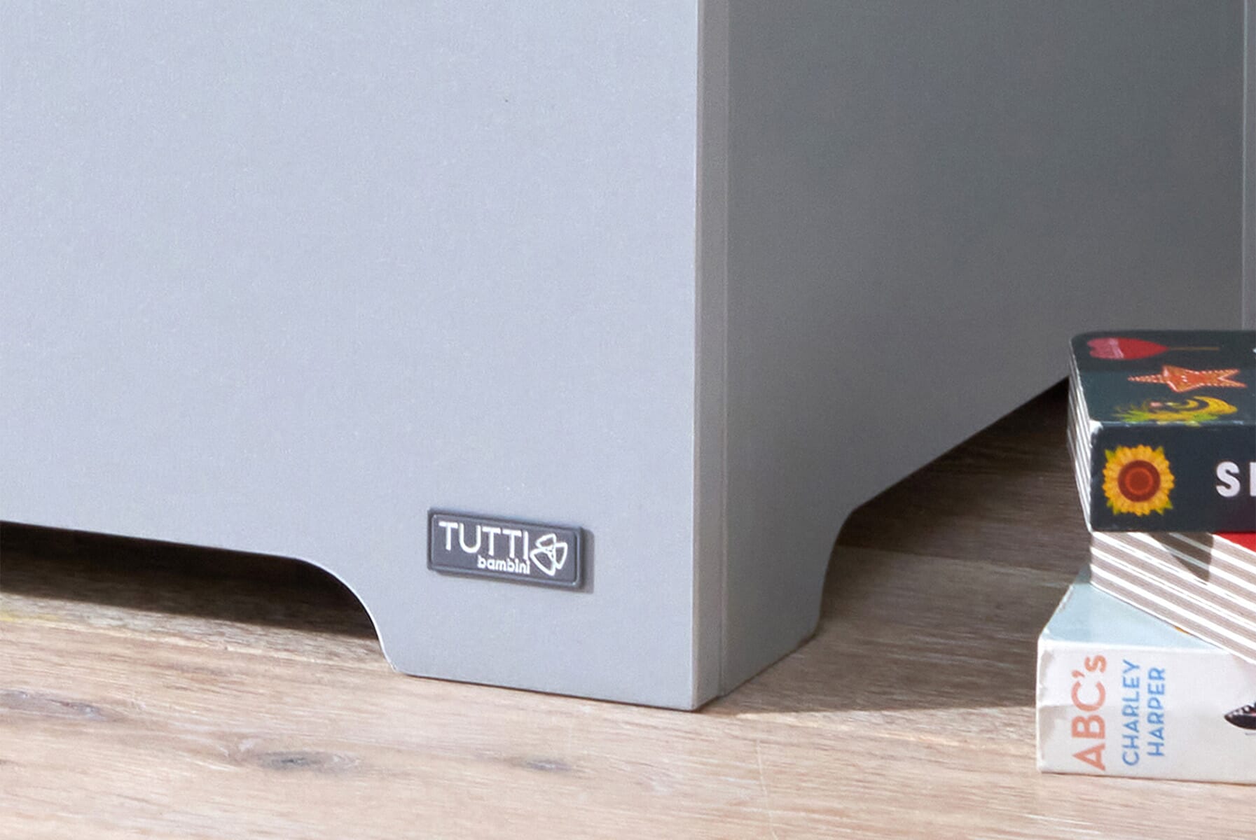 Close-up of the Modena toy box in dove grey and oak highlighting the Tutti Bambini logo and smooth panel detailing on the lower corner