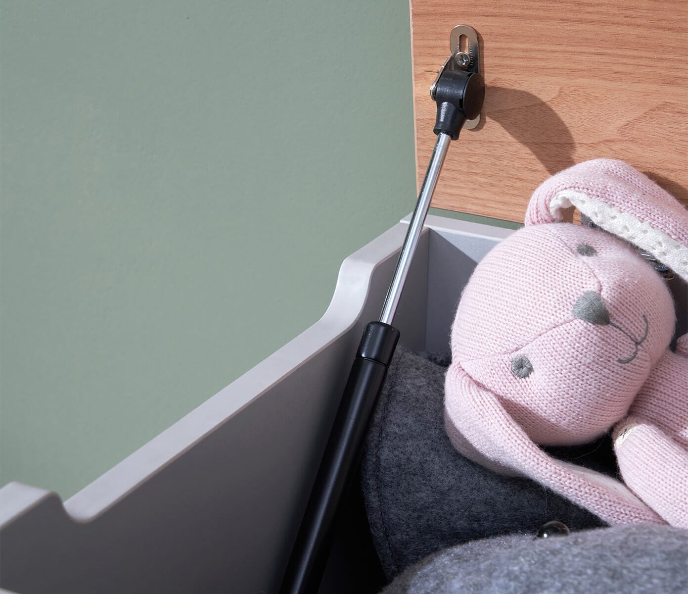 Detailed view of the Modena toy box’s soft-close hinge in dove grey and oak, showing safe, controlled lid movement beside plush toys