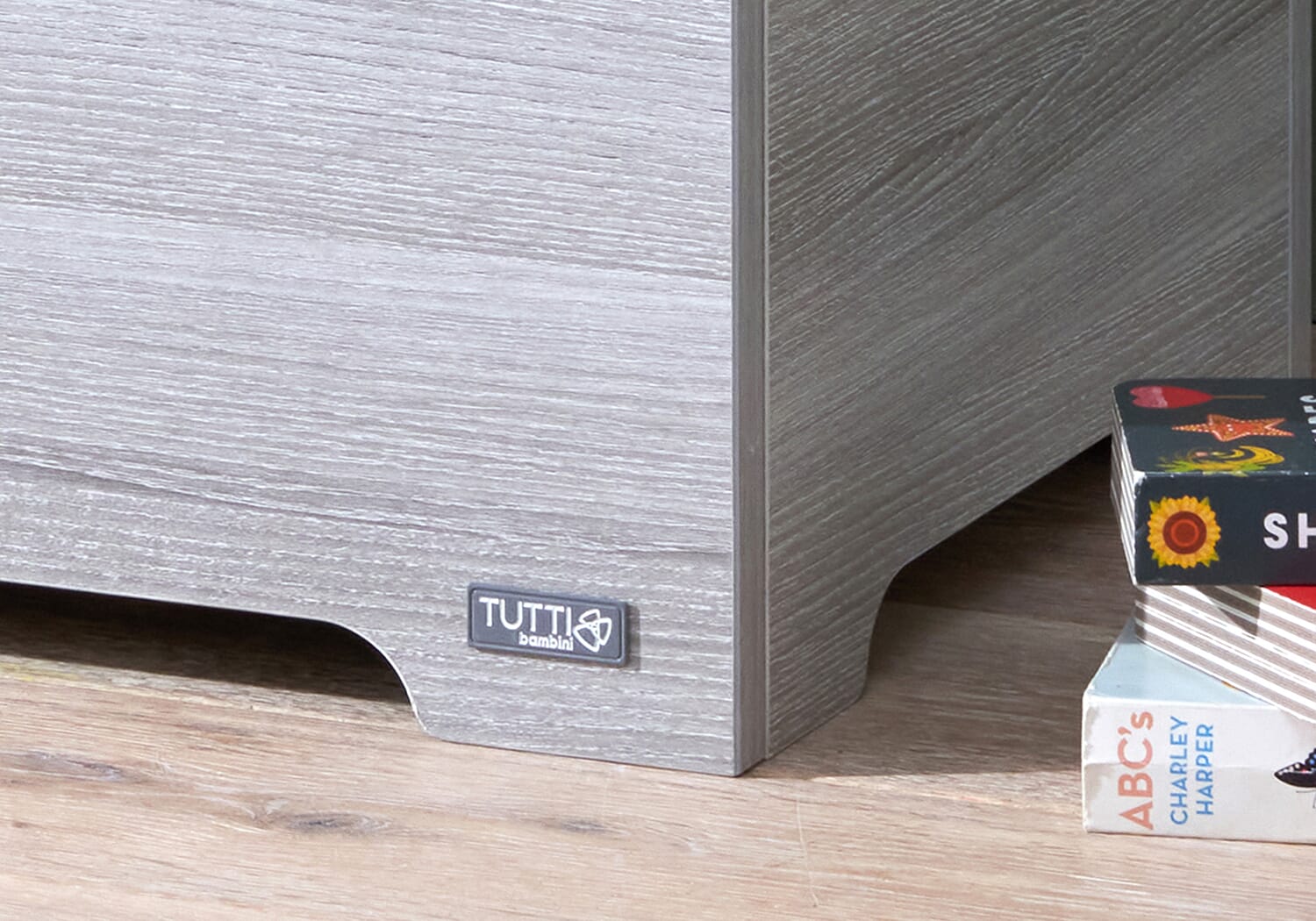 Close-up of the Modena toy box in grey ash showing the Tutti Bambini logo and textured woodgrain finish on the front panel