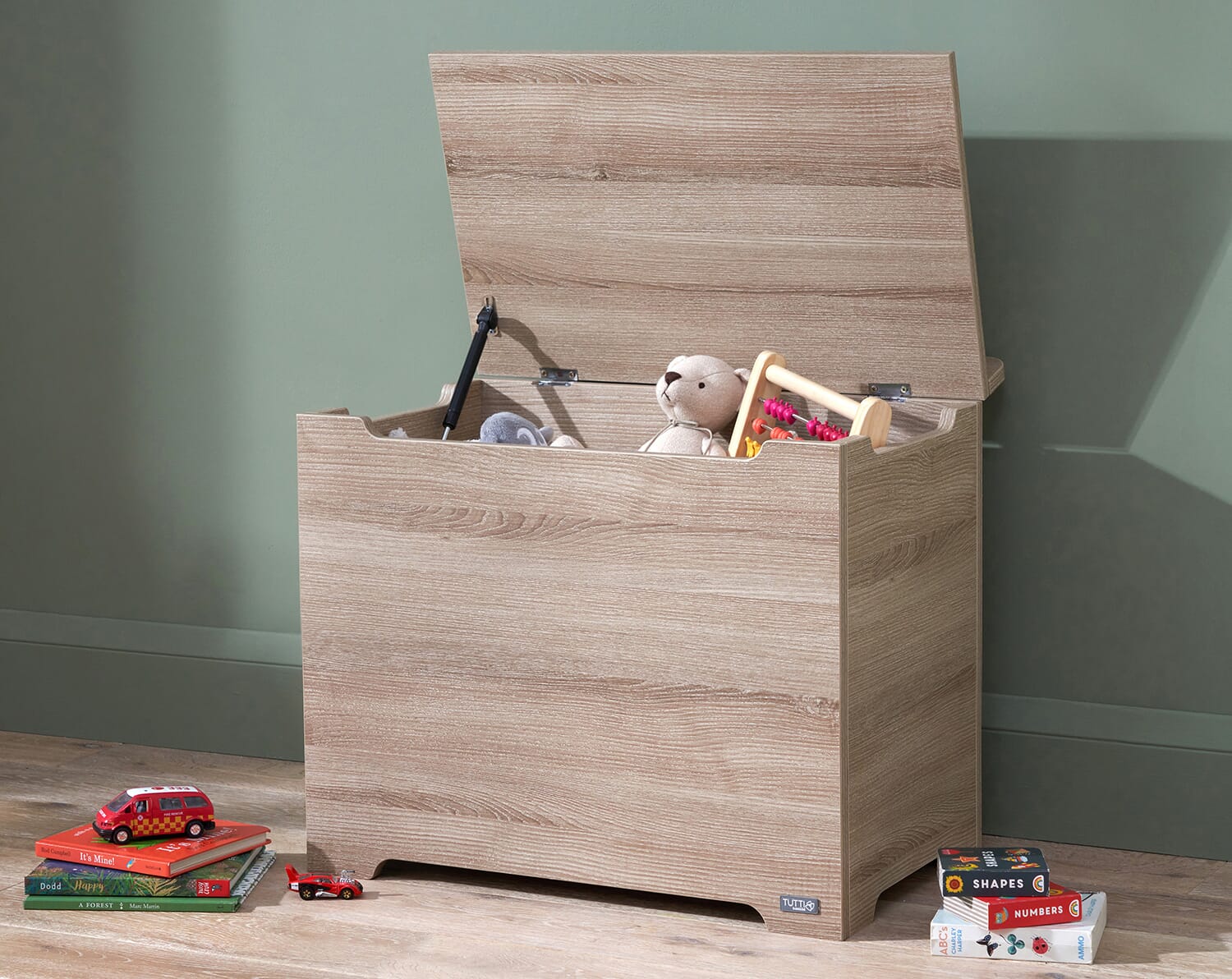 Oak Modena toy box with the lid open, showing a soft-close hinge and spacious interior filled with toys against a calm nursery backdrop
