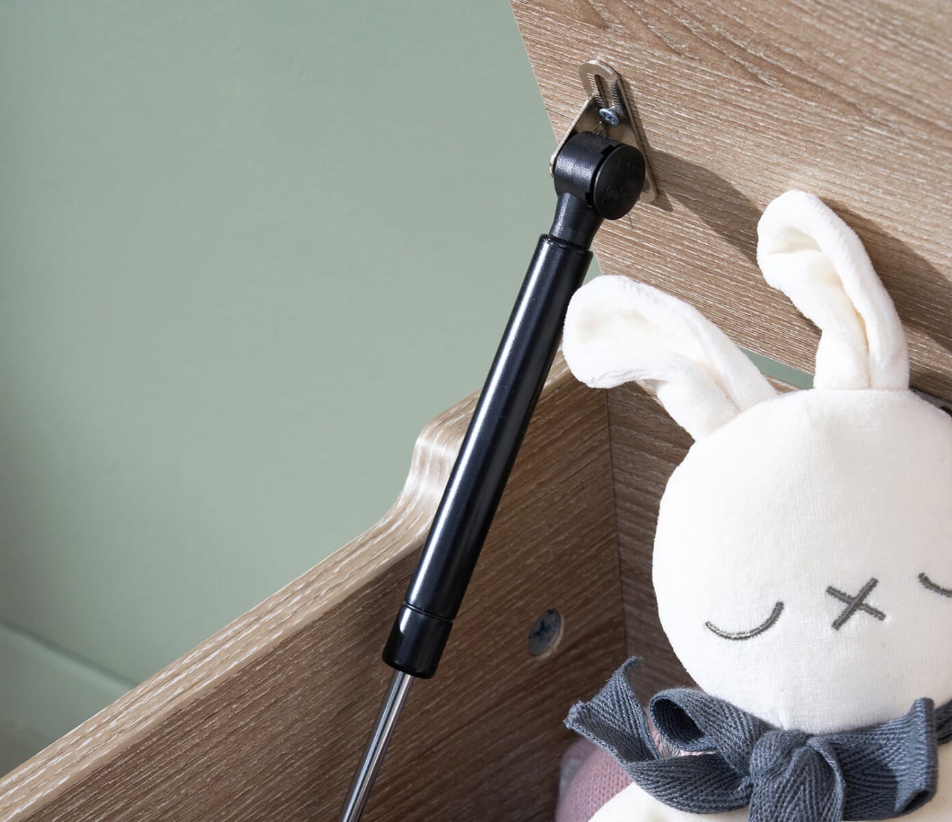 Detailed view of the Modena oak toy box hinge mechanism, showing the soft-close support arm beside a plush toy inside the box