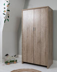 Modena wardrobe in oak finish shown in a child's bedroom with doors closed, featuring a warm wood grain texture and compact design for stylish and practical nursery storage.