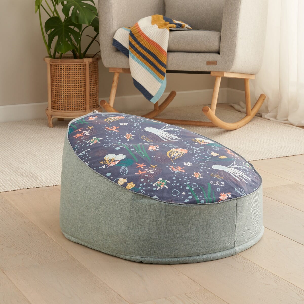Our Planet baby beanbag styled in a calm nursery setting, featuring ocean-themed print, soft green fabric and a supportive cocooned shape