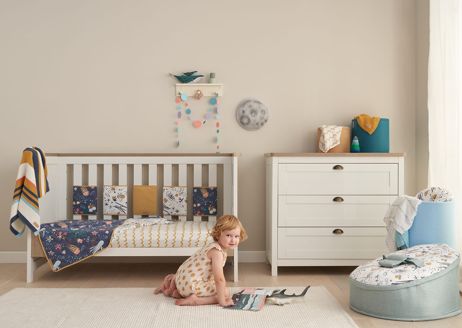 Our Planet themed nursery with cot, felt wall décor and mobile, styled with soft ocean prints and a baby playing on the floor