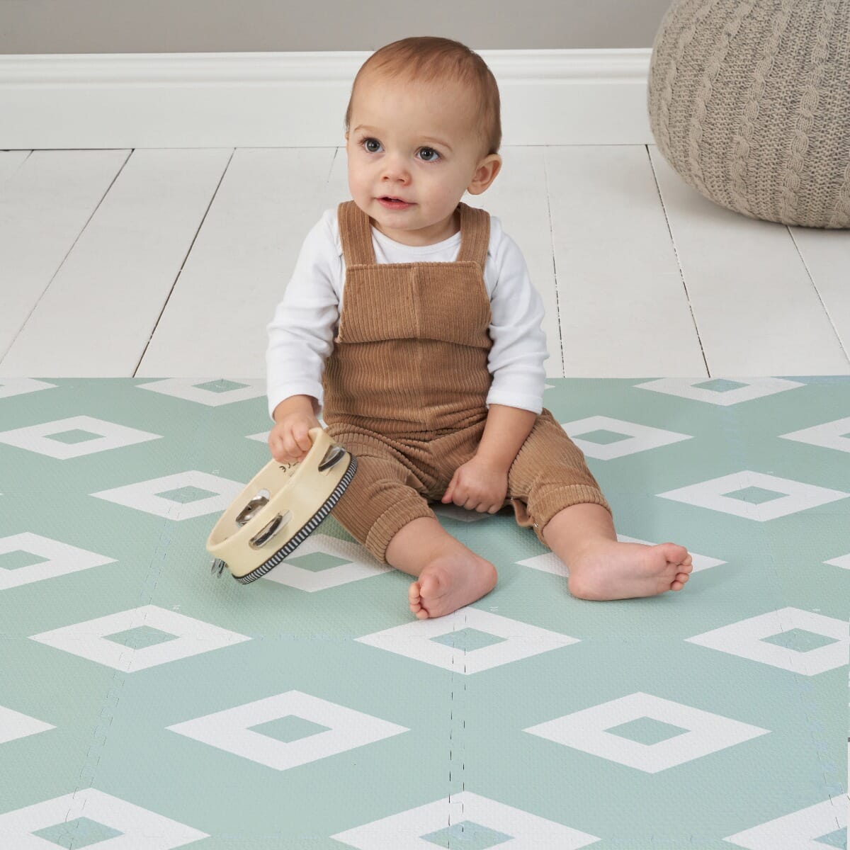 Toddler sitting on the diamond mint puzzle playmat, holding a tambourine, showing the cushioned surface designed for safe floor play