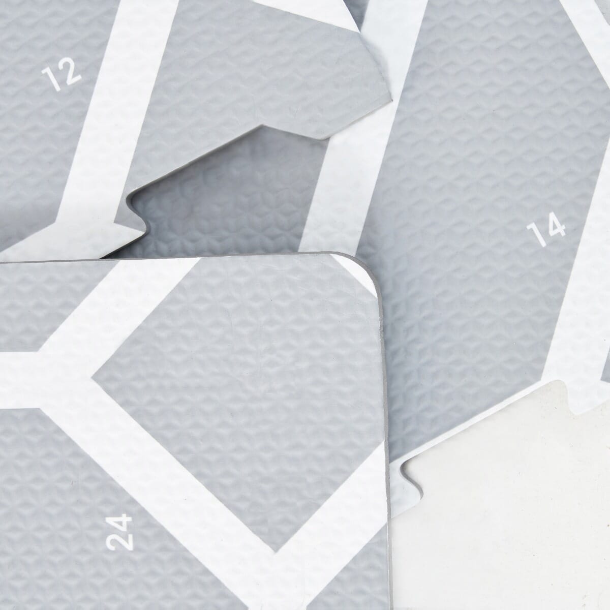 Close-up of grey puzzle playmat tiles showing textured surface, numbered edges and white geometric pattern for guided assembly