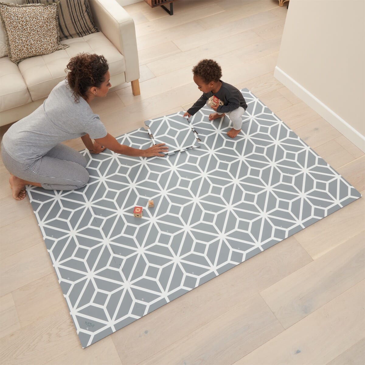 Parent and toddler assembling grey geometric puzzle tiles, showing the mat’s modular design and spacious cushioned area for play and learning