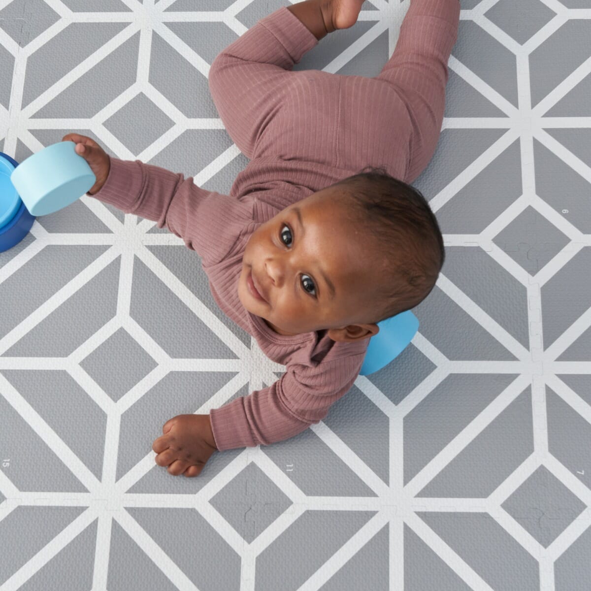 Baby playing on grey geometric puzzle tiles, highlighting the soft, supportive surface designed for comfortable tummy time and early play