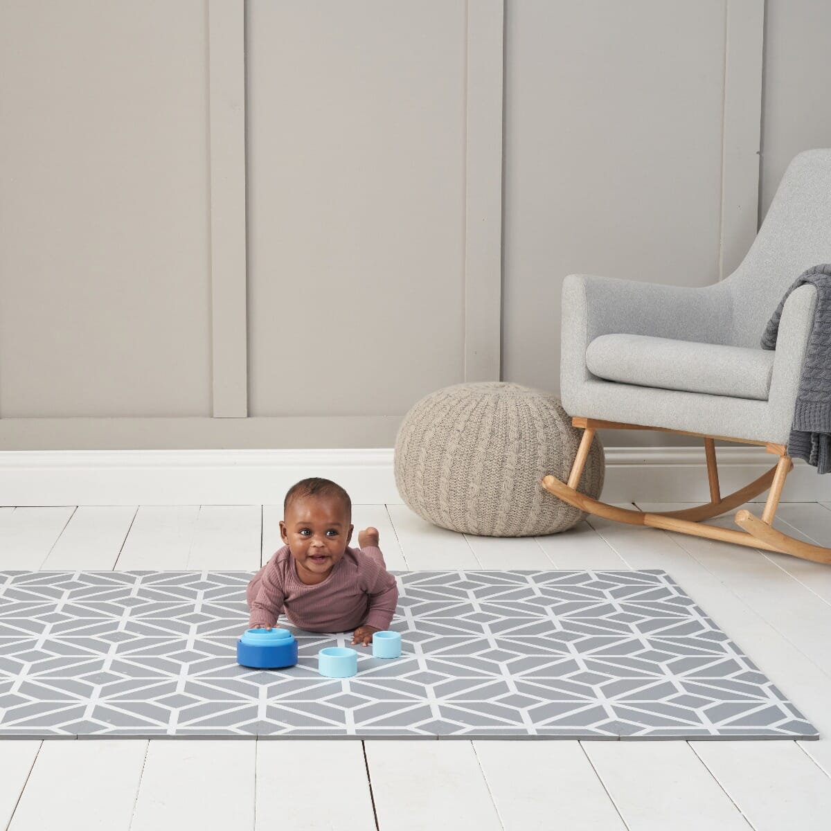 Baby playing on grey geometric puzzle playmat, showing soft cushioned surface that supports tummy time and early developmental play