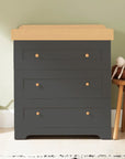 Rio chest changer in slate with honey oak top styled in a nursery, featuring three roomy drawers and a removable changing tray