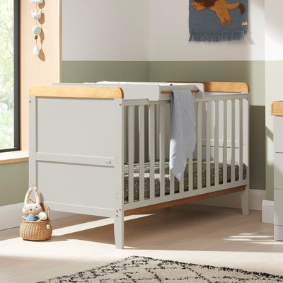 Rio cot bed in dove grey and oak with cot top changer, styled in a soft green nursery with natural wood accents, showcasing its contemporary aesthetic and space-saving design.