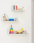 Nursery lifestyle view of Rio L-shaped wall shelves in dove grey mounted on a white wall, styled with colourful toys and books for practical and decorative storage.