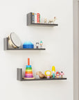 Lifestyle image of Rio set of three L-shaped wall shelves in slate grey mounted on nursery wall with toys, demonstrating decorative and functional display use.