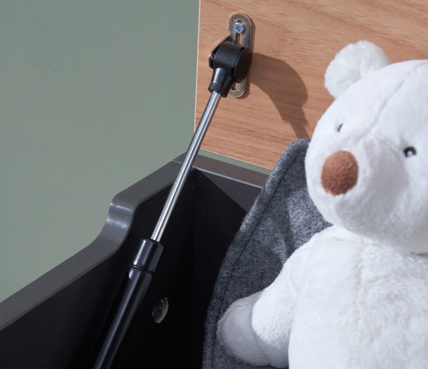 Close-up of the Rio toy box in slate grey and honey oak showing the soft-close hinge mechanism beside a plush teddy for safe, gentle use