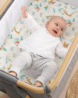 Baby lying on Run Wild bedside crib fitted sheet, organic cotton with playful jungle animal prints offering softness and a snug fit