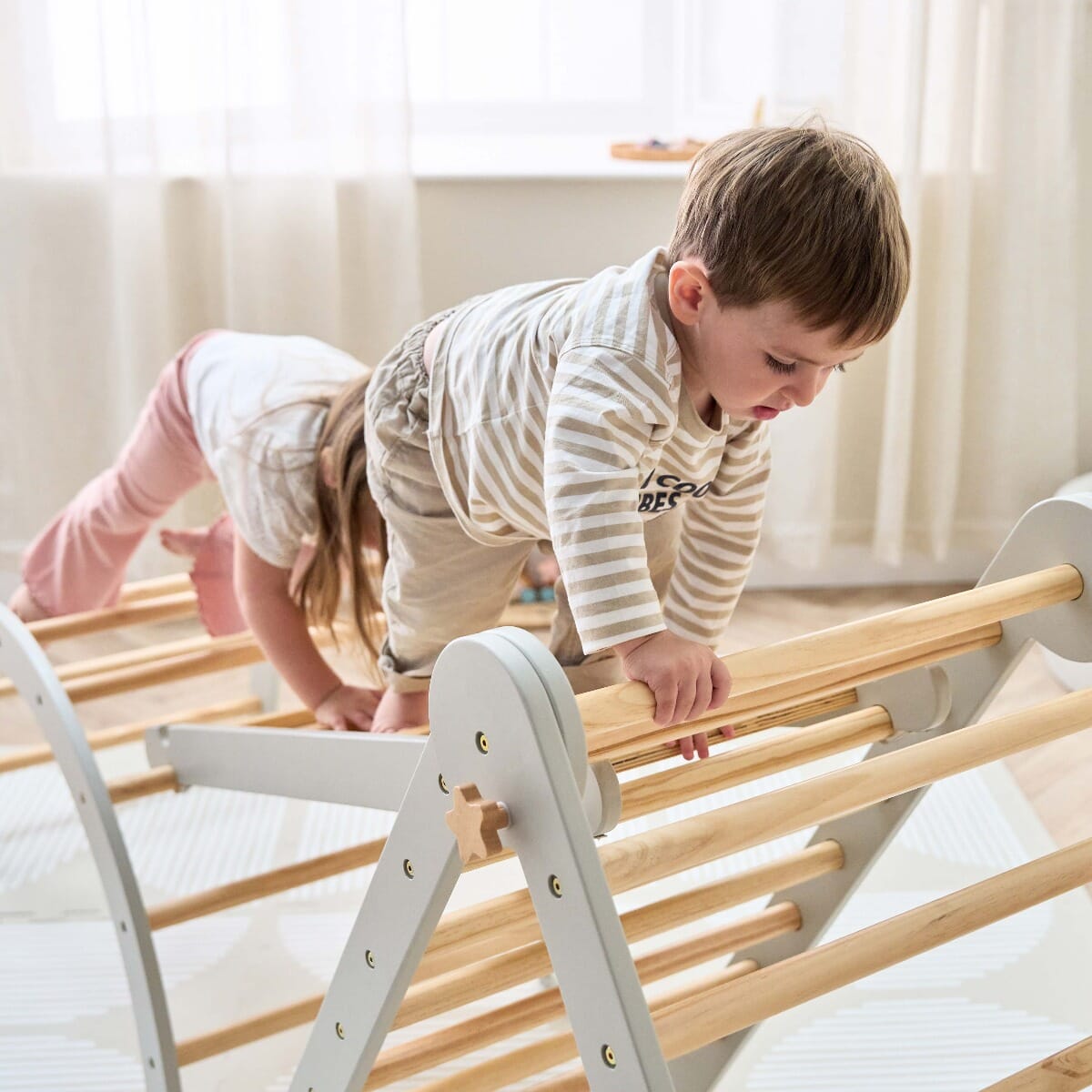 Two children actively climbing the Scala Montessori Pikler frame in mushroom finish, encouraging strength, balance, and coordination