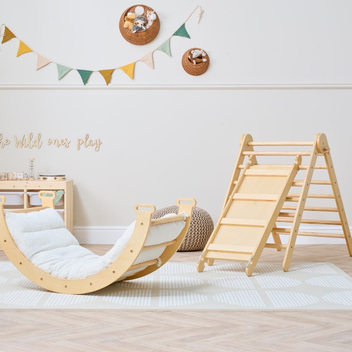 Natural wood climbing frame with slide and arch rocker with cushion shown in a playroom setting