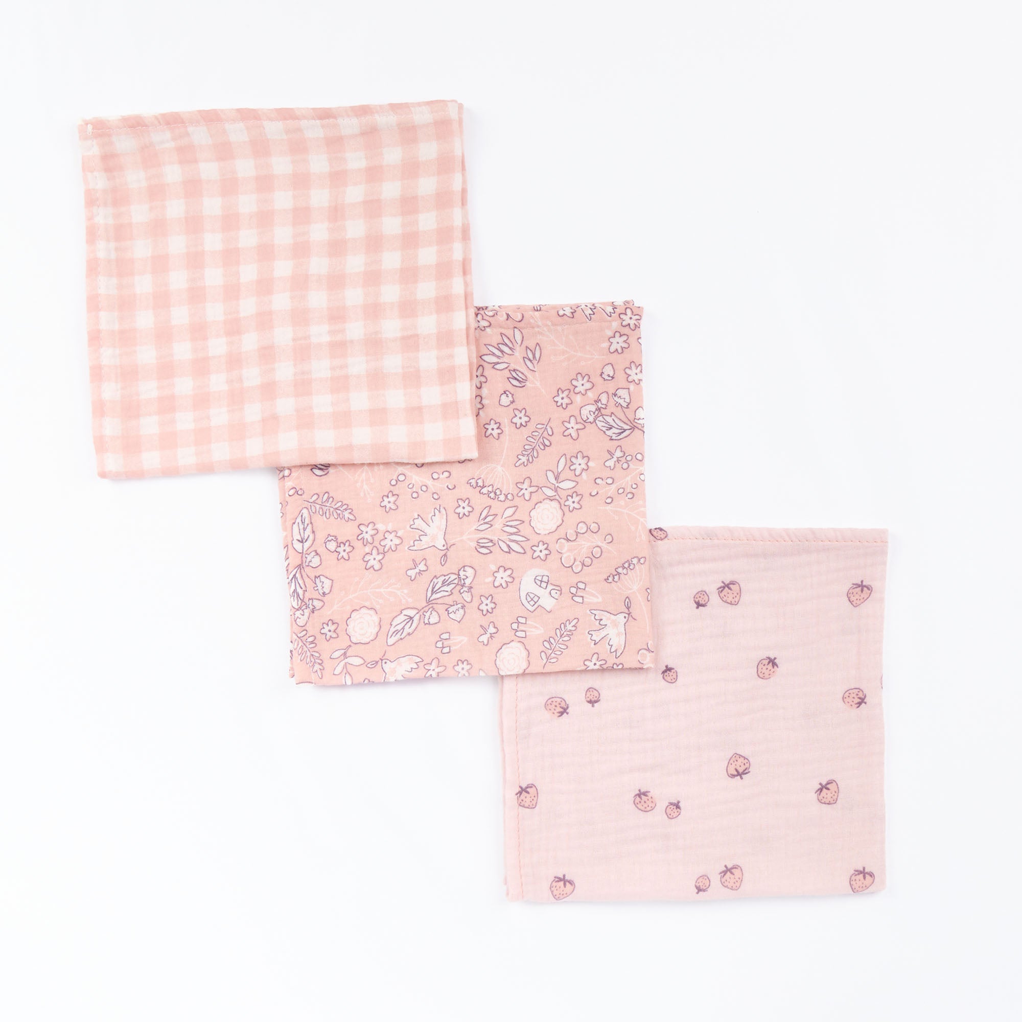 Flat lay of three Tiny Tails large muslin square swaddles in pink floral, gingham, and strawberry prints, highlighting soft cotton muslin weave