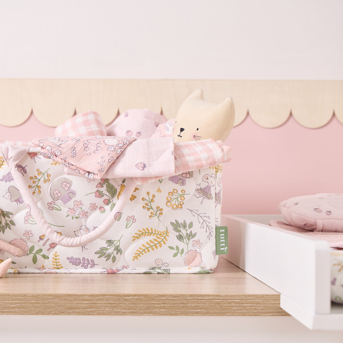 Close-up of the Tiny Tails nappy caddy in pink floral woodland print, styled on a nursery shelf with soft toys and muslin cloths