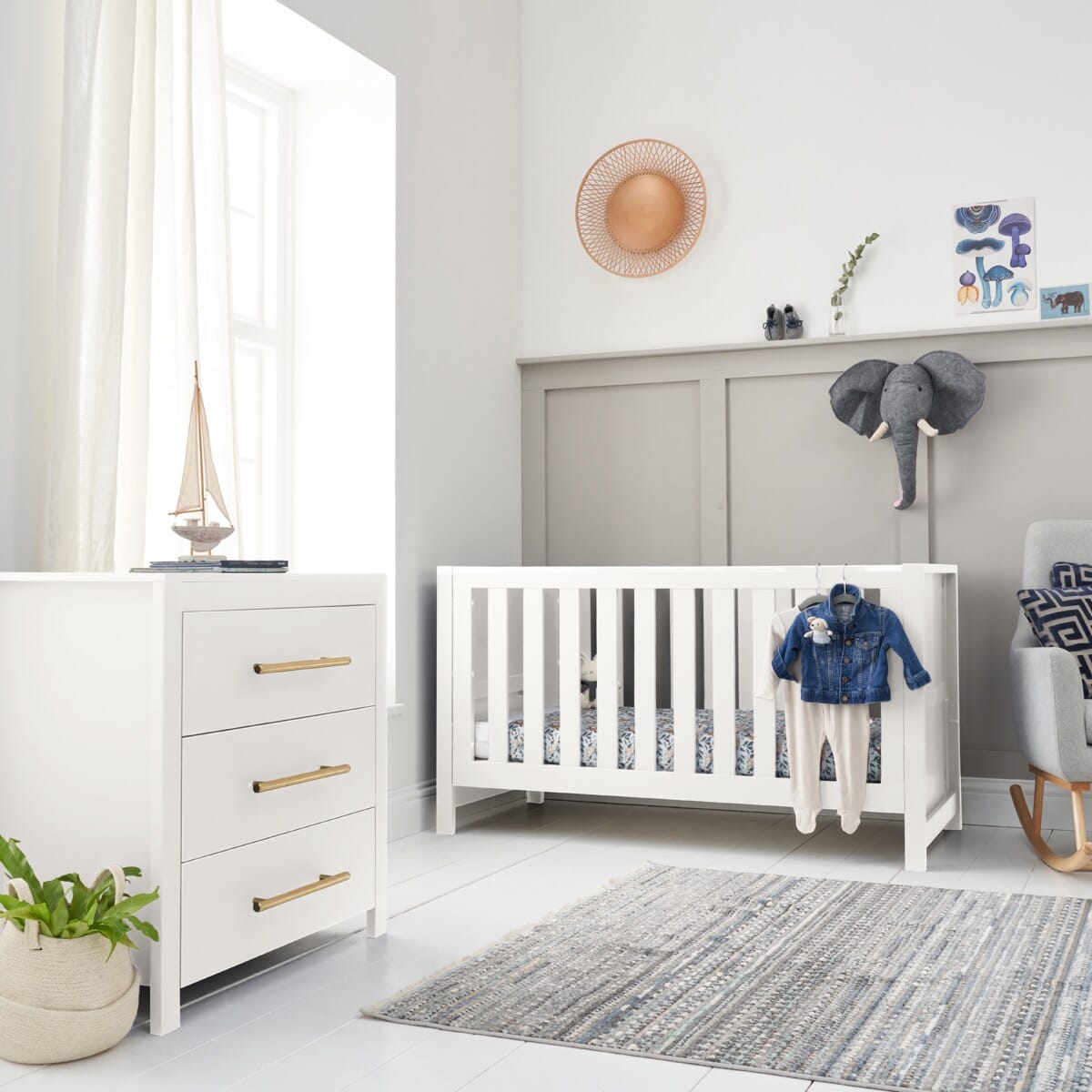 Tivoli white two-piece nursery room set consisting of a cot bed and a chest of drawers, displayed in a room with various children's decorative items.