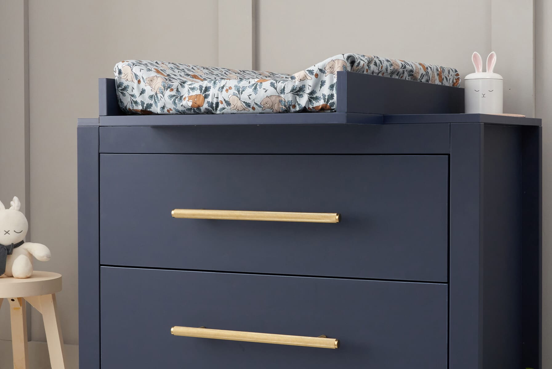 Close-up of the Tivoli chest changer in navy with gold handles and changing top, highlighting smooth lines and a calm, modern nursery setup