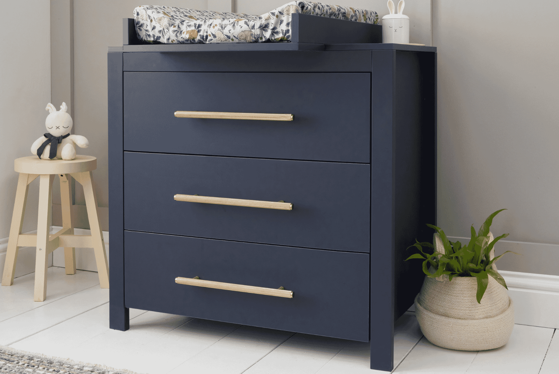 Close-up lifestyle view of the Tivoli chest changer in navy with brushed gold handles and changing top, styled with soft nursery accents